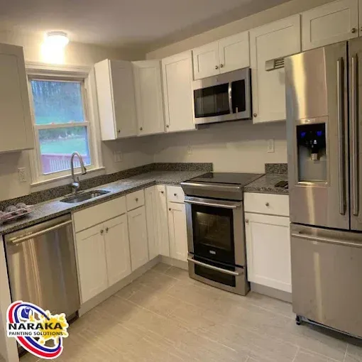 Modern white kitchen with stainless steel appliances, granite countertops, and light gray tiled floors.