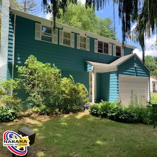 Teal house with white trim, shutters, and garage door on a sunny day.