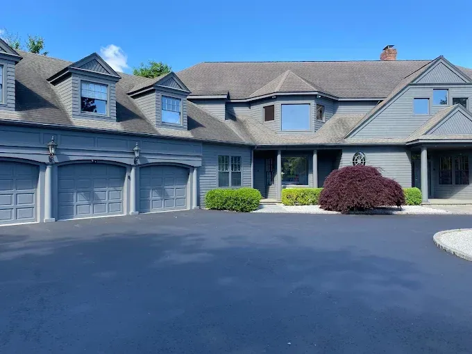 Blue house with three-car garage, driveway, and landscaping on a sunny day.