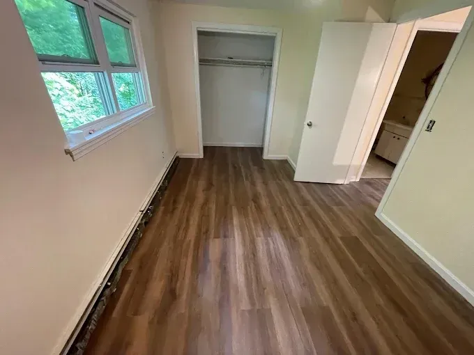 Empty room with wood-look flooring, a closet, window, and two open doors to other rooms.