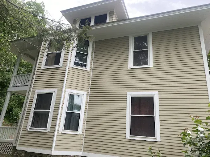 Two-story beige house with white trim. Windows on side, porch on left.