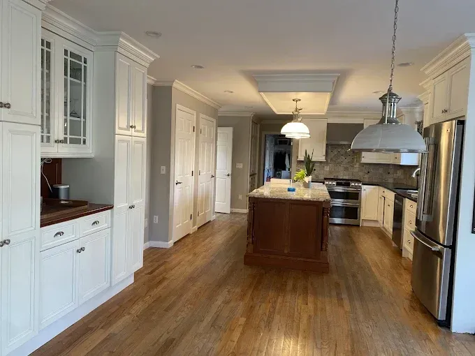 Spacious kitchen with white cabinets, dark wood island, stainless steel appliances, and wood flooring.