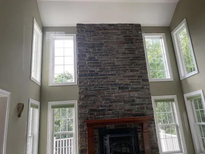 Stone fireplace with windows on either side. Tall ceiling with sage green walls.