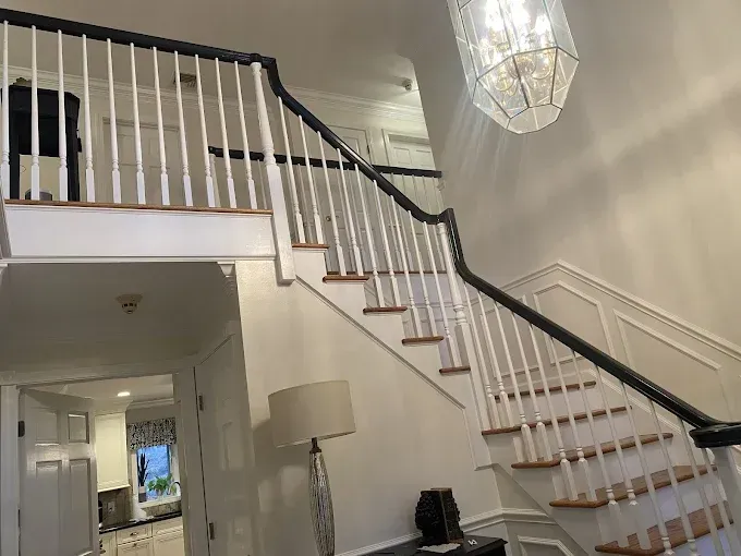 Interior staircase with white spindles, black handrails, and a hanging chandelier.