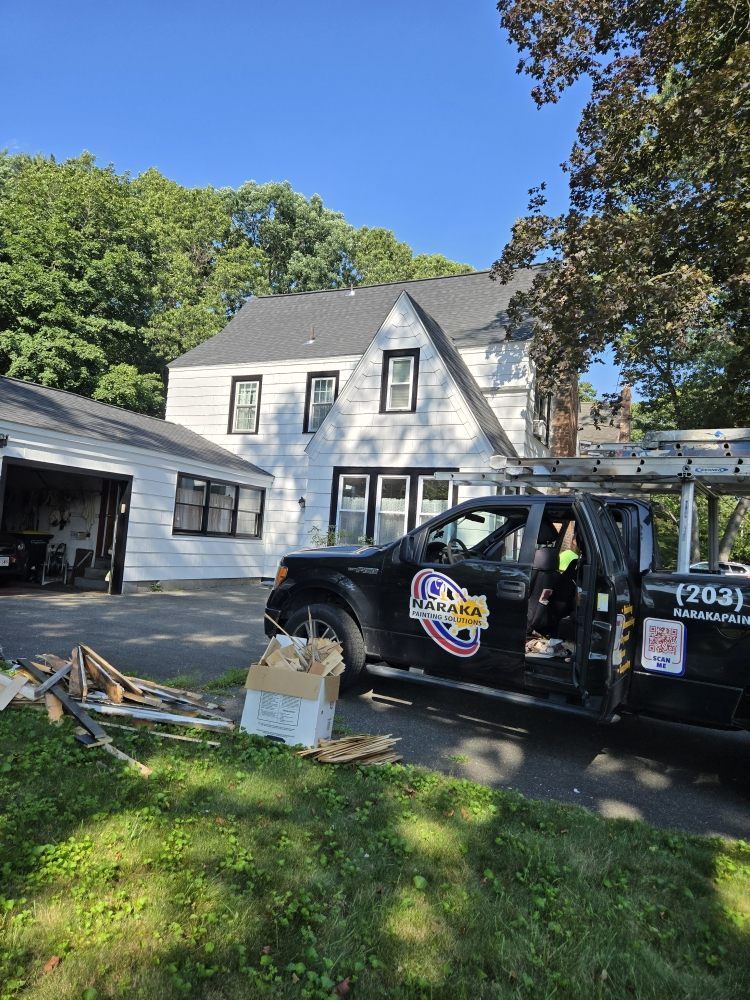 White house with black trim, a work truck parked in front, and a ladder on the roof.