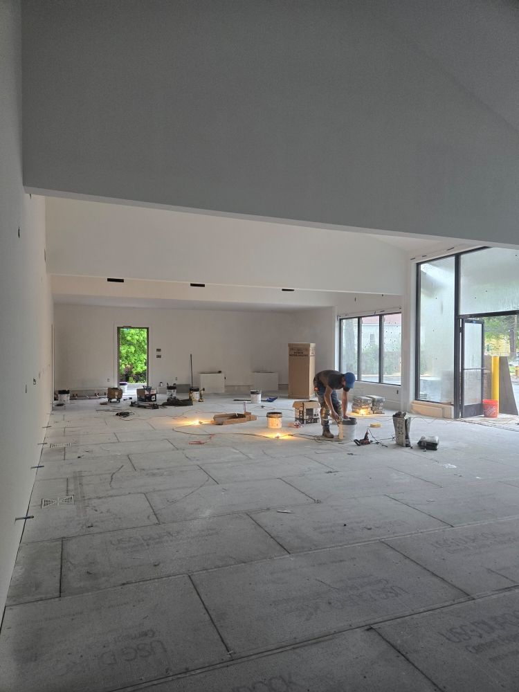 Construction worker installing flooring in a bright, open room with windows.