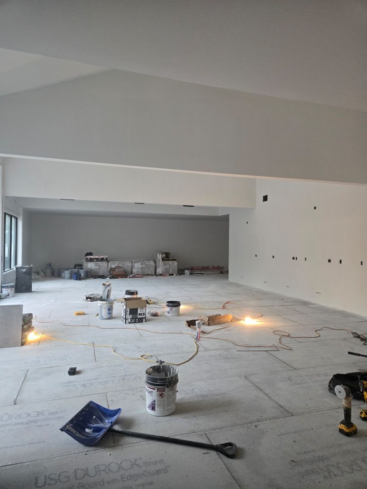 Interior construction site with gray walls and flooring, tools scattered, and bare electrical outlets.