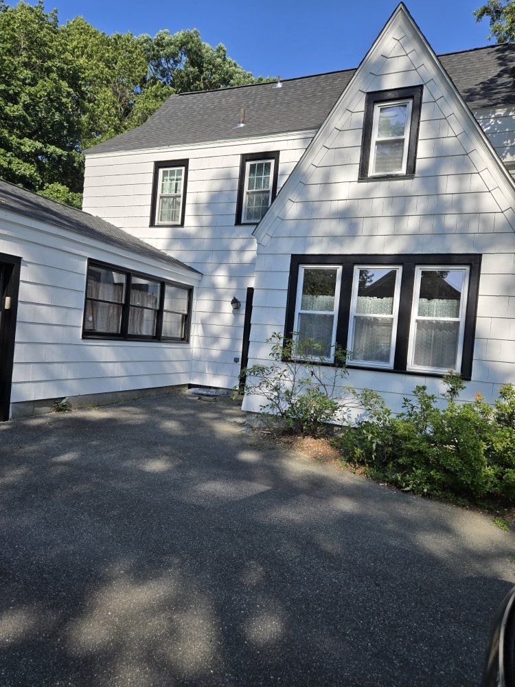 White house with black-framed windows and a dark driveway. Sunlight shines on the building and grounds.