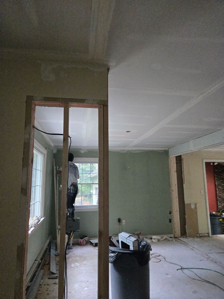 Interior renovation in progress. Man on a ladder near window. Unfinished walls and ceiling.
