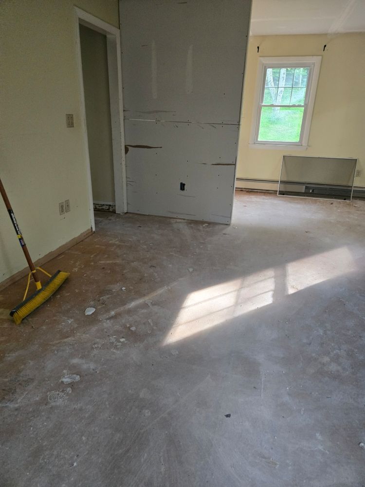 Room with debris-covered floor, doorway, window, and half-wall. A yellow broom rests on the floor.