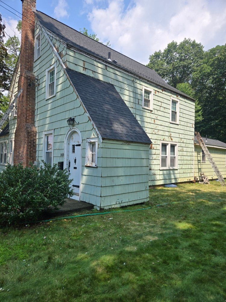 Green house with black roof and a brick chimney on a grassy lawn.