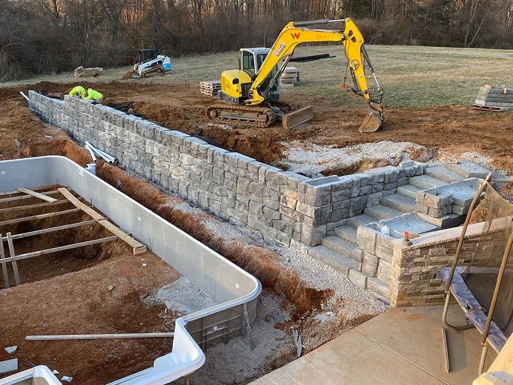 A yellow excavator is working on a construction site next to a pool.