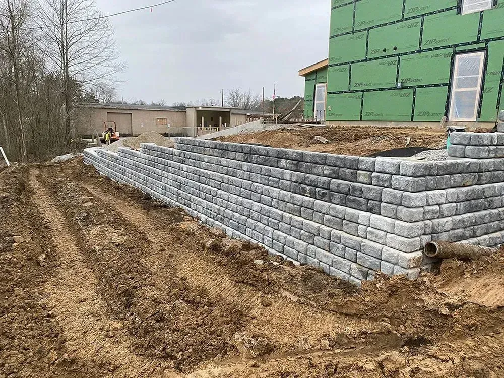 Retaining wall made of gray blocks, holding back dirt, next to a house under construction with
green