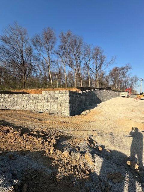 A person is standing in a dirt field with a brick wall in the background.