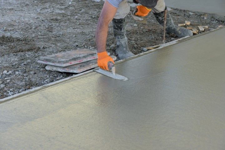Worker smoothing a freshly poured concrete slab with a trowel