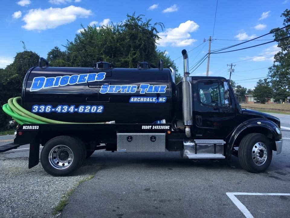 A black septic tank truck is parked in a parking lot