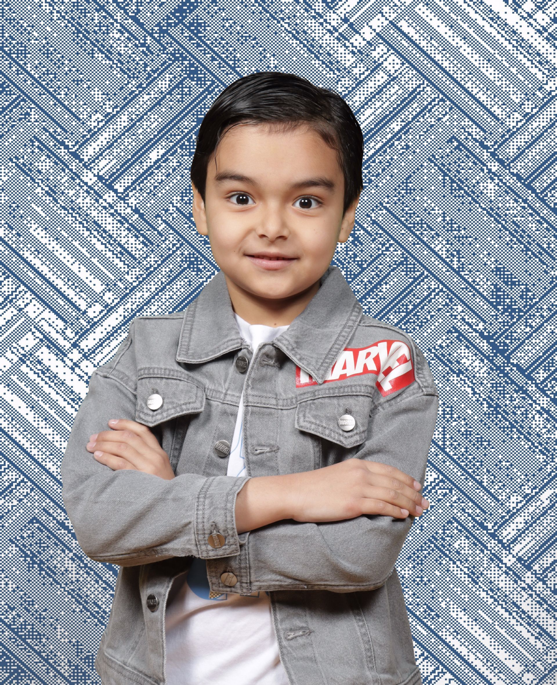 A young boy wearing a denim jacket and a white shirt is standing with his arms crossed.