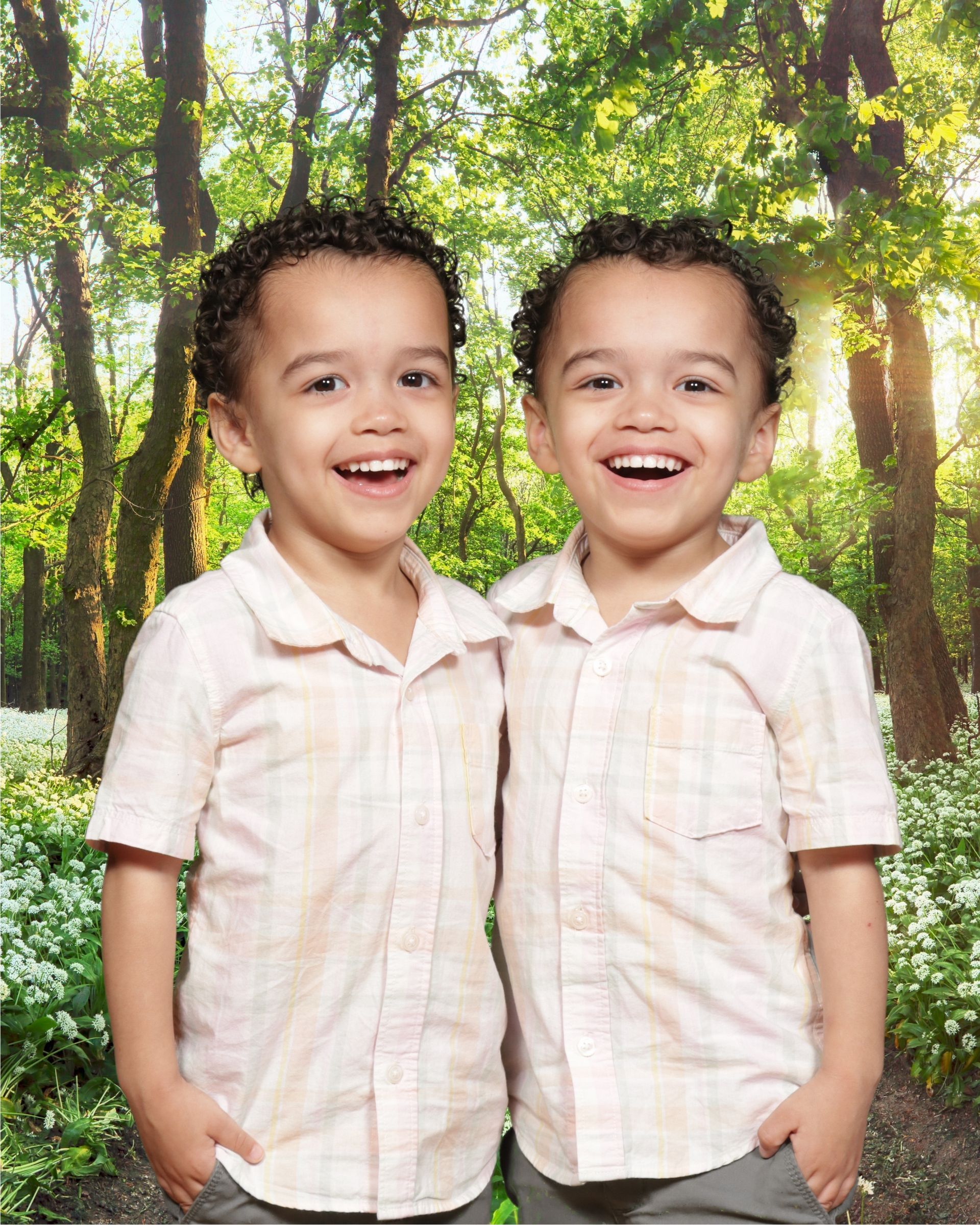 Two young boys are standing next to each other in a forest.