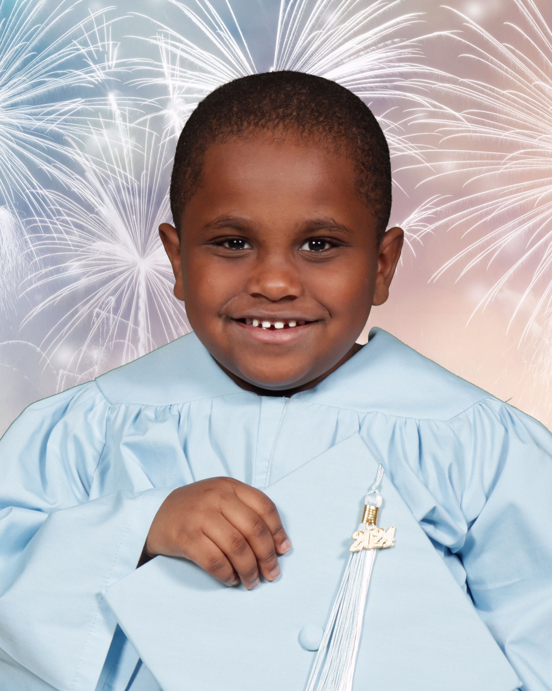 A young boy in a graduation cap and gown is smiling in front of fireworks