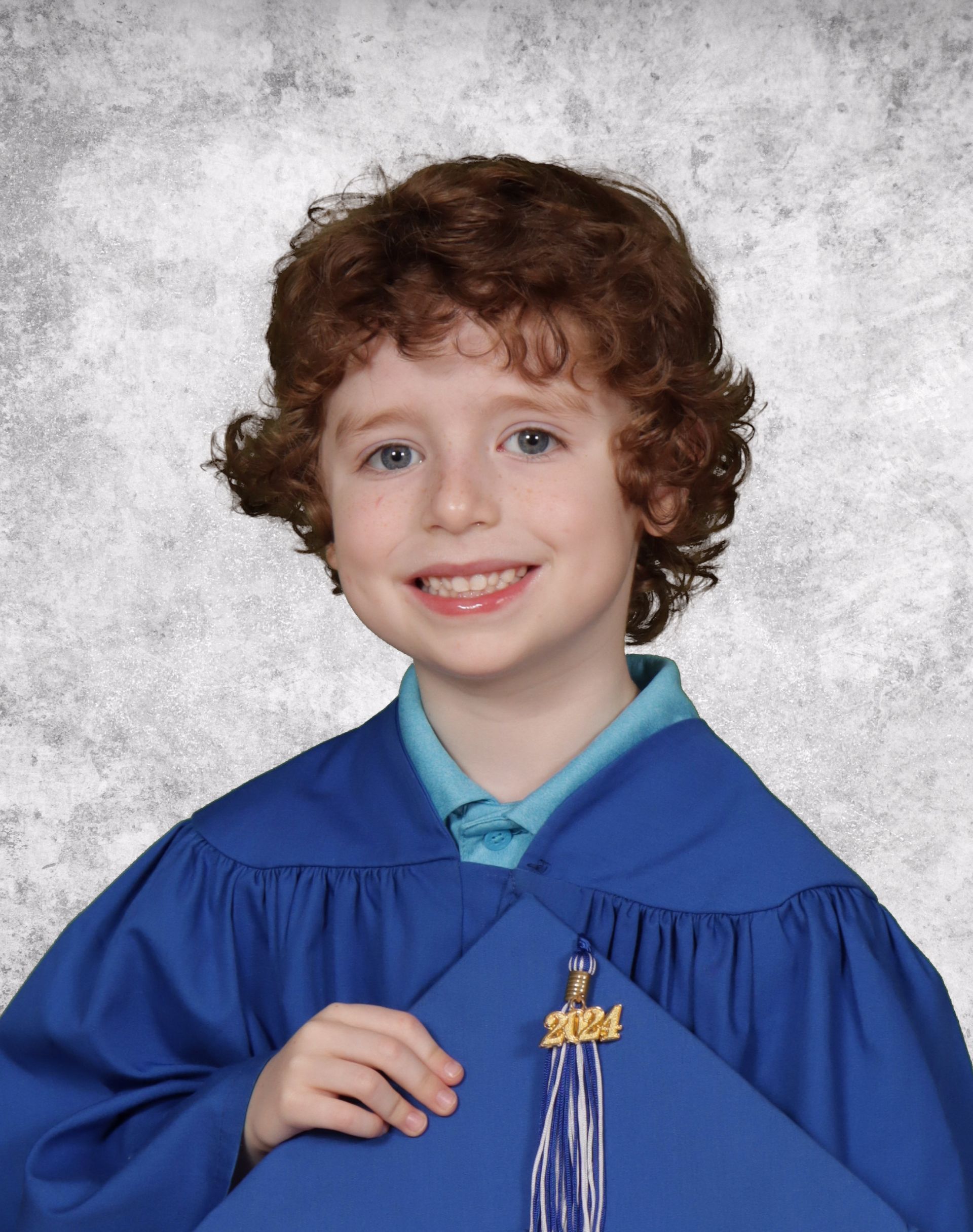 A young boy in a blue gown is holding a diploma