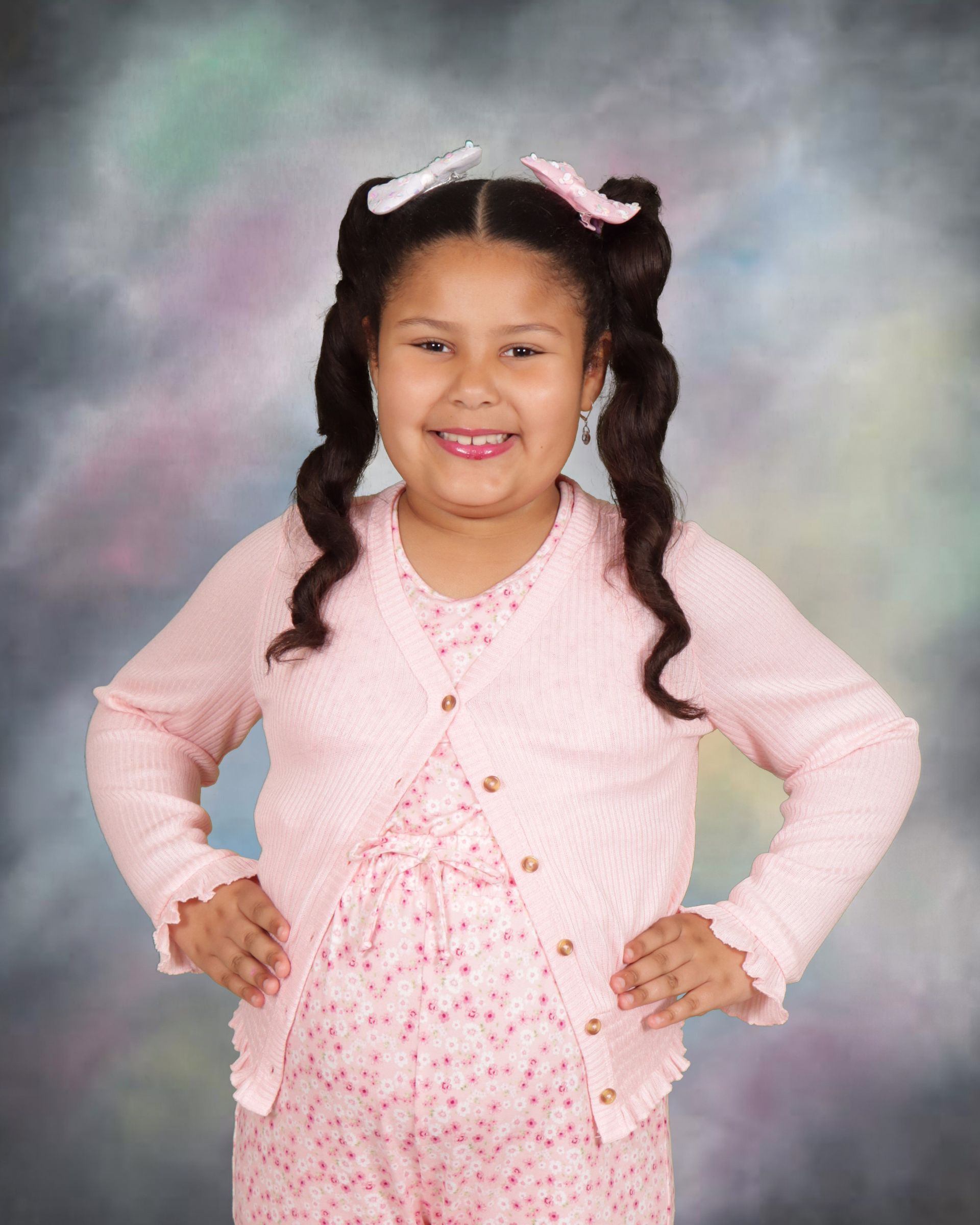 A little girl wearing a pink cardigan and a pink dress