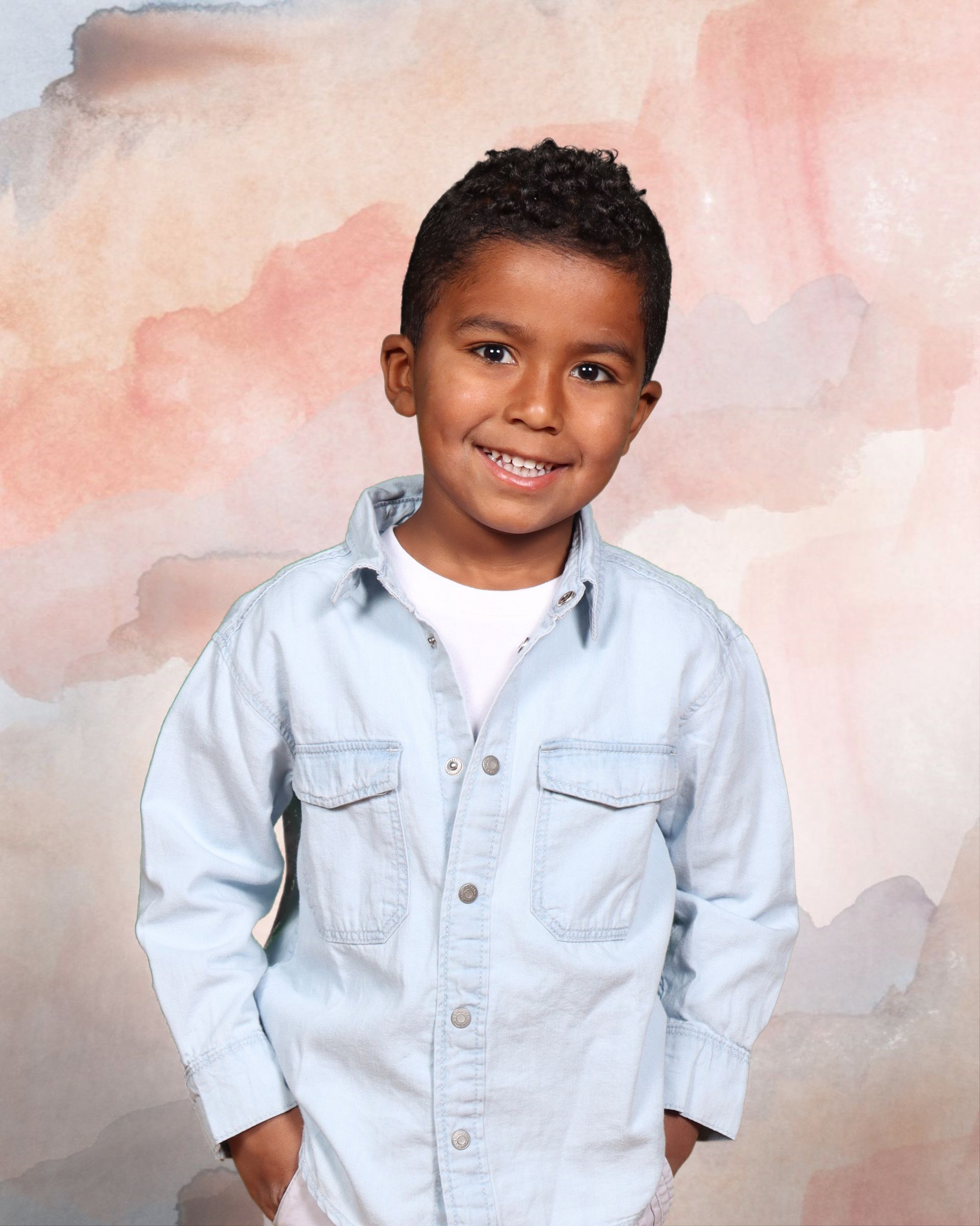 A young boy with his hands in his pockets smiles for the camera