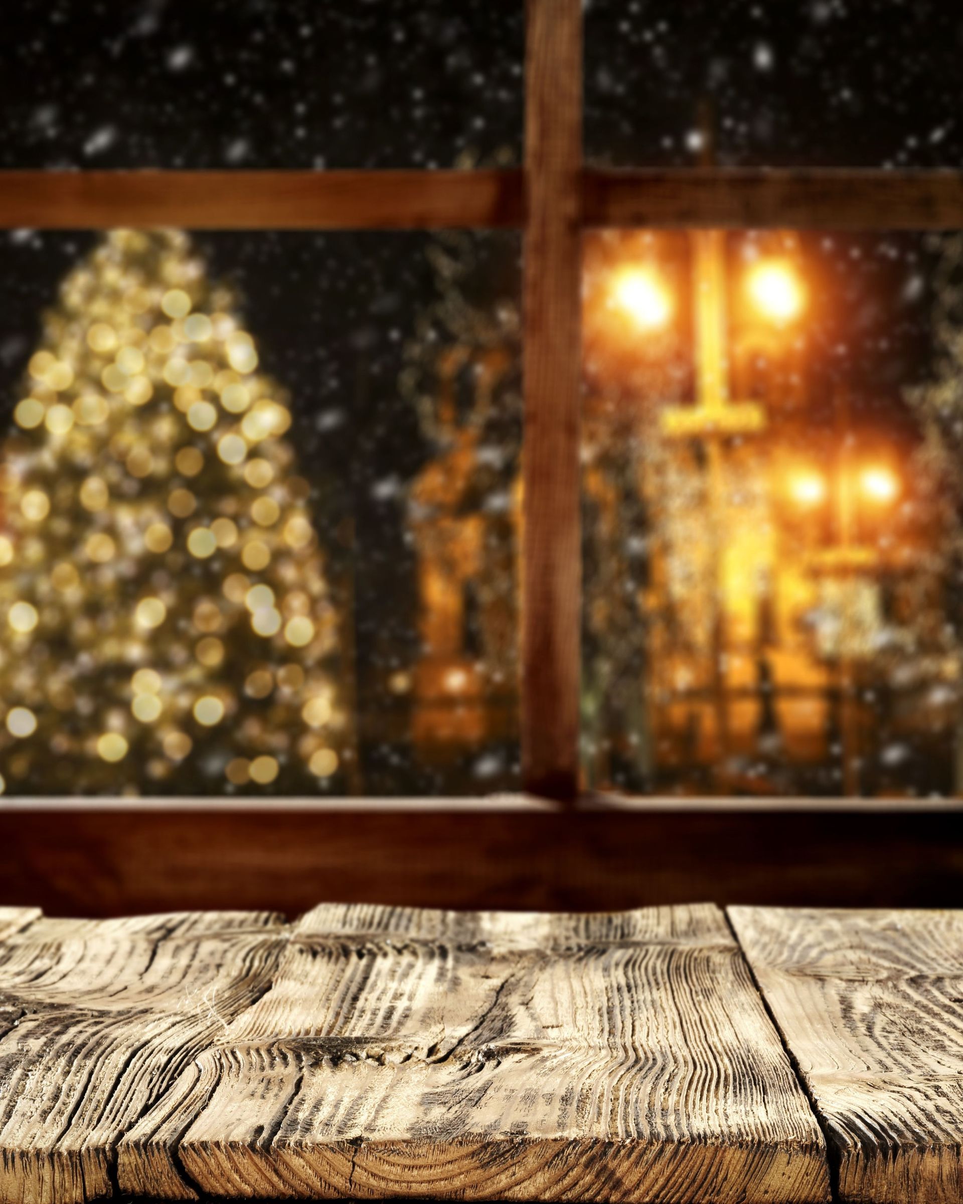 A wooden table in front of a window with a christmas tree in the background.