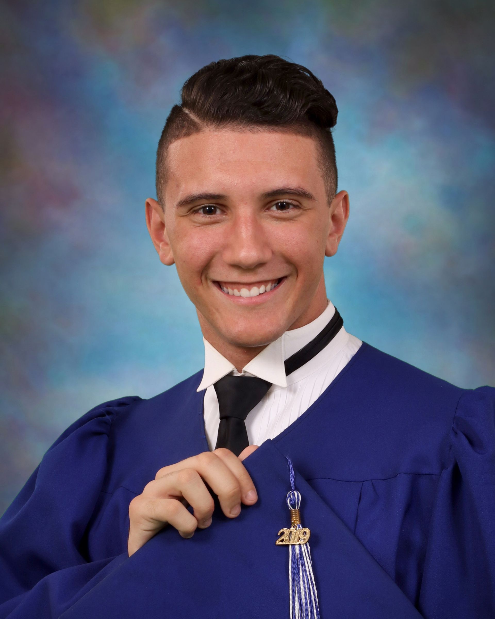 A young man in a graduation cap and gown is smiling for the camera.