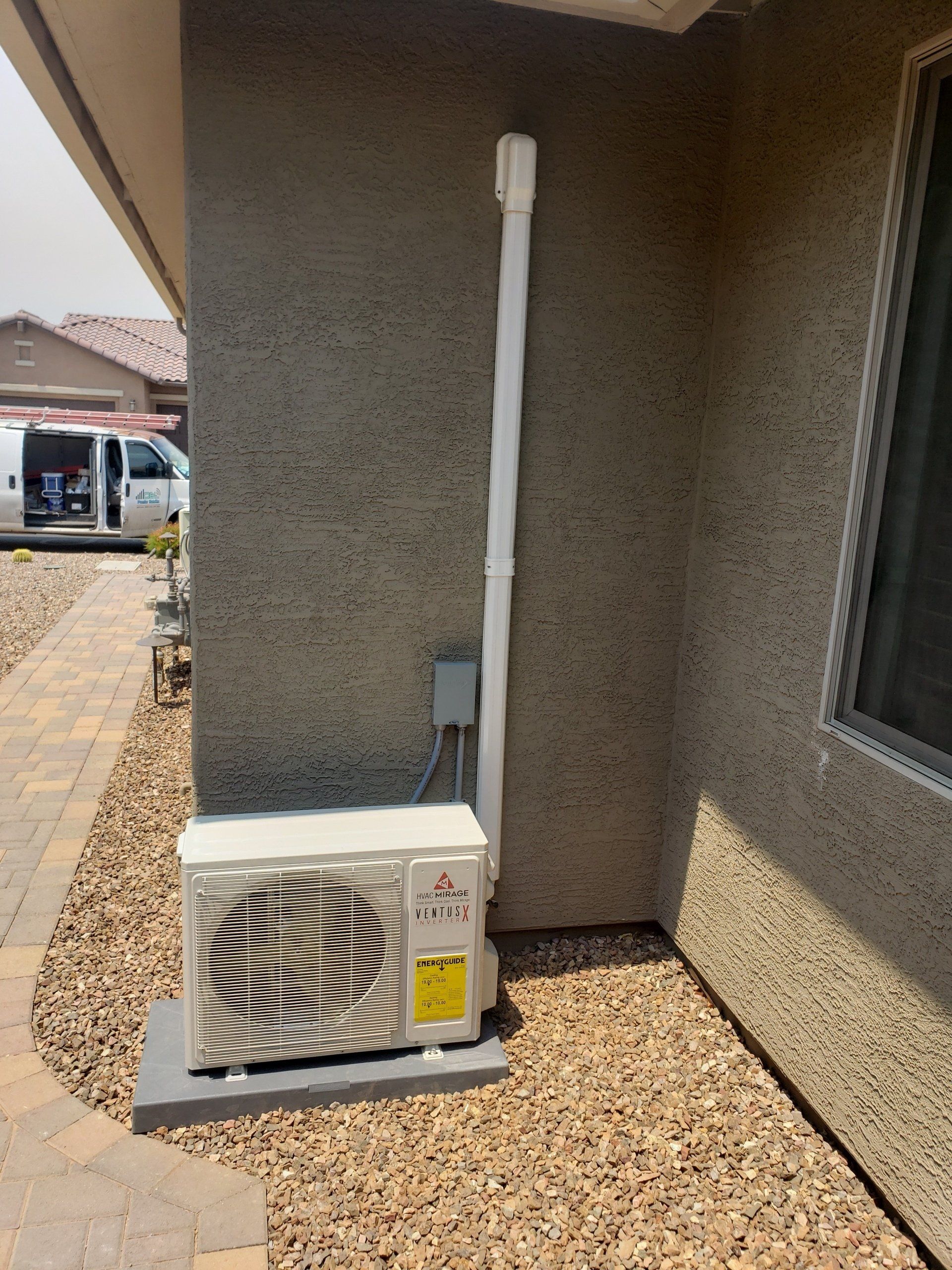Outdoor air conditioning unit against a stucco wall, with a white vent pipe and electrical box.