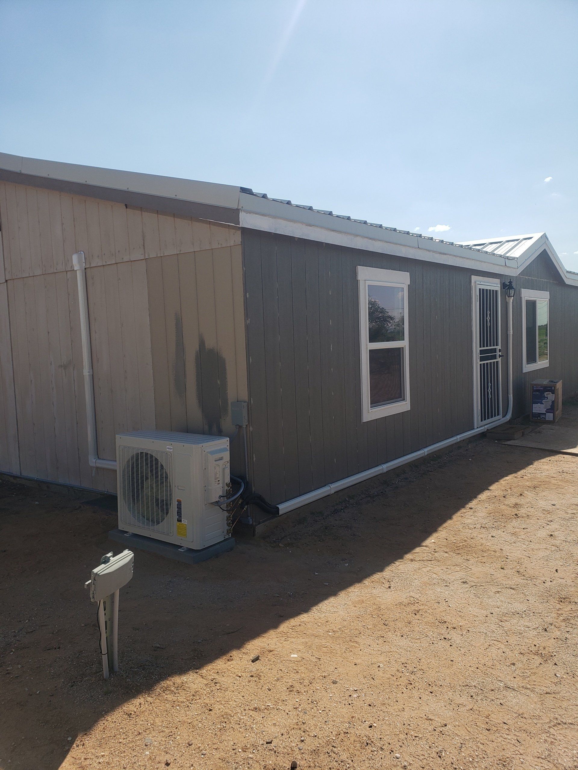 Exterior view of a small building with gray siding, white trim, and a wall-mounted air conditioning unit.