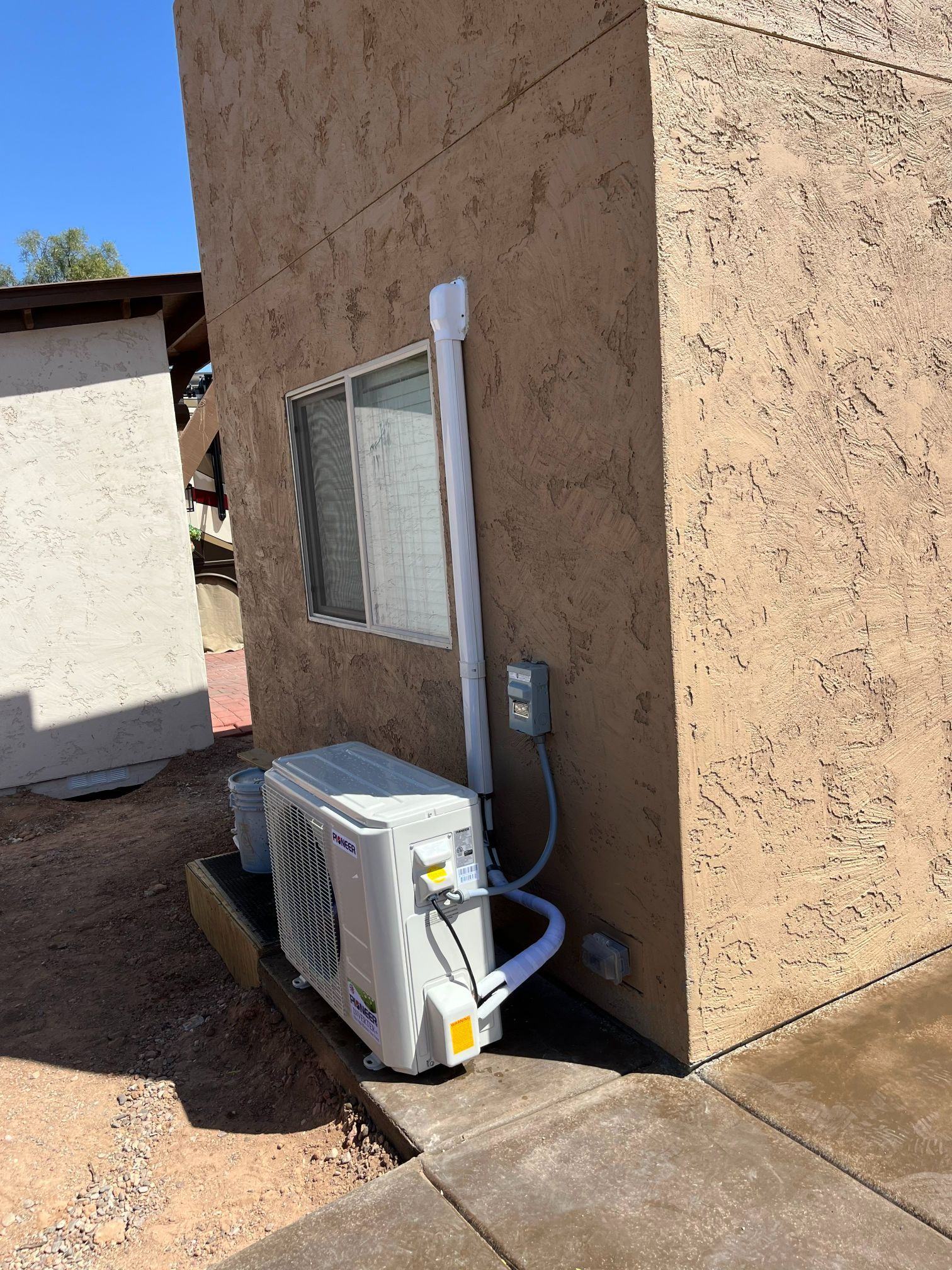 An air conditioning unit next to a building with a window and electrical components.