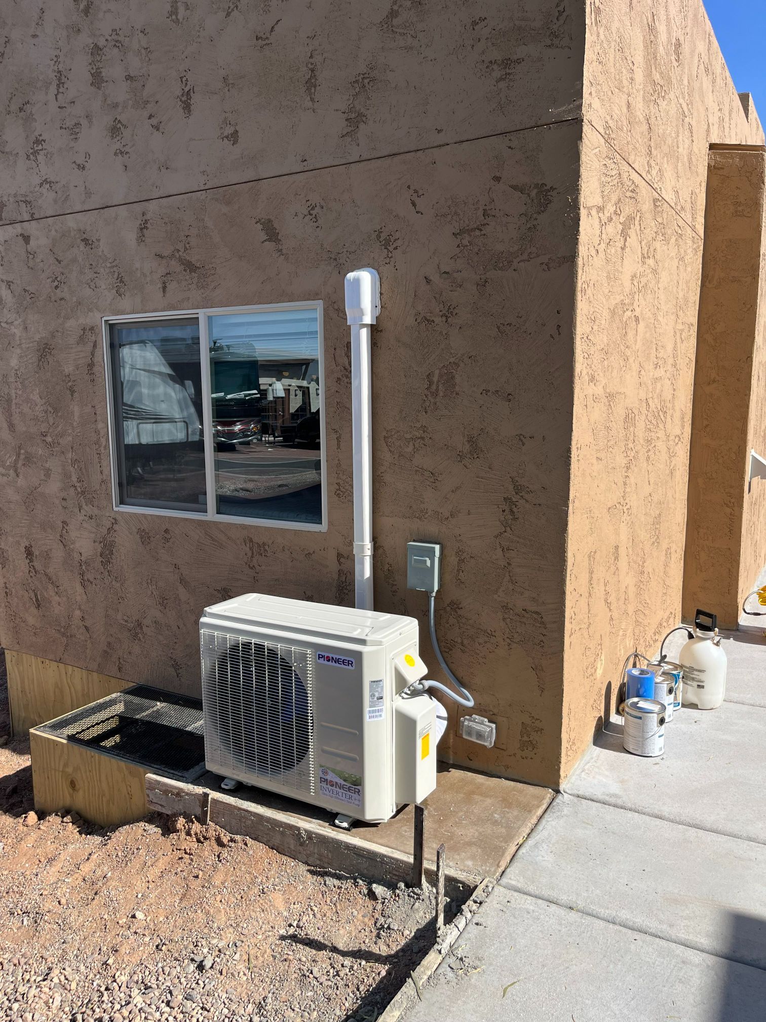 Exterior view of a building with an air conditioning unit installed next to a window. A white pipe extends upward.