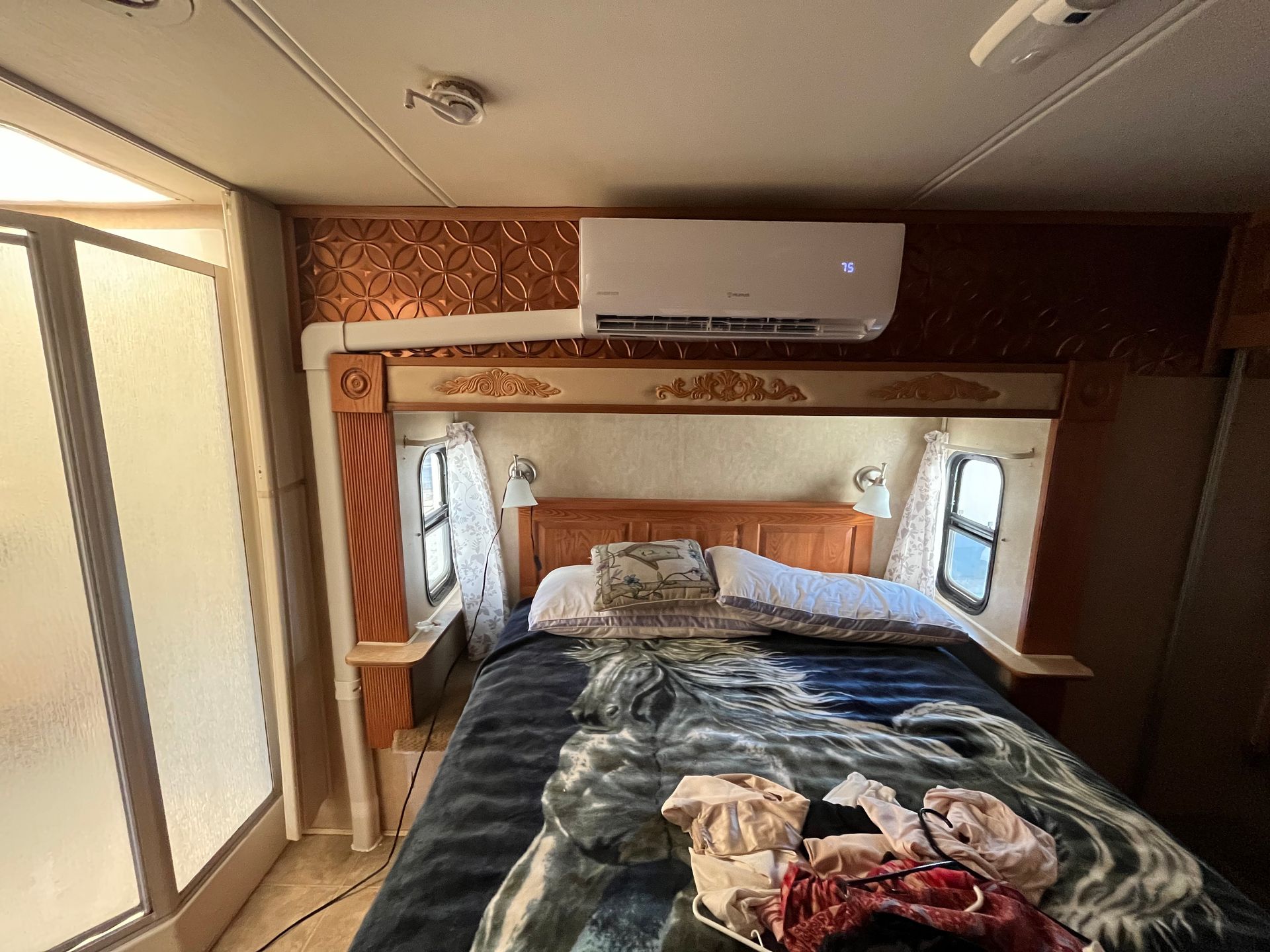 RV bedroom with a bed, shower, and mounted air conditioner.