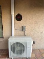White AC unit against stucco wall, with electrical conduit and a small round wall decoration.