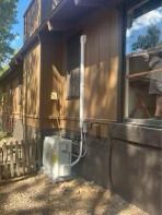 Gas meter and vent pipe installed on the exterior of a brown building, near a window and wooden fence.