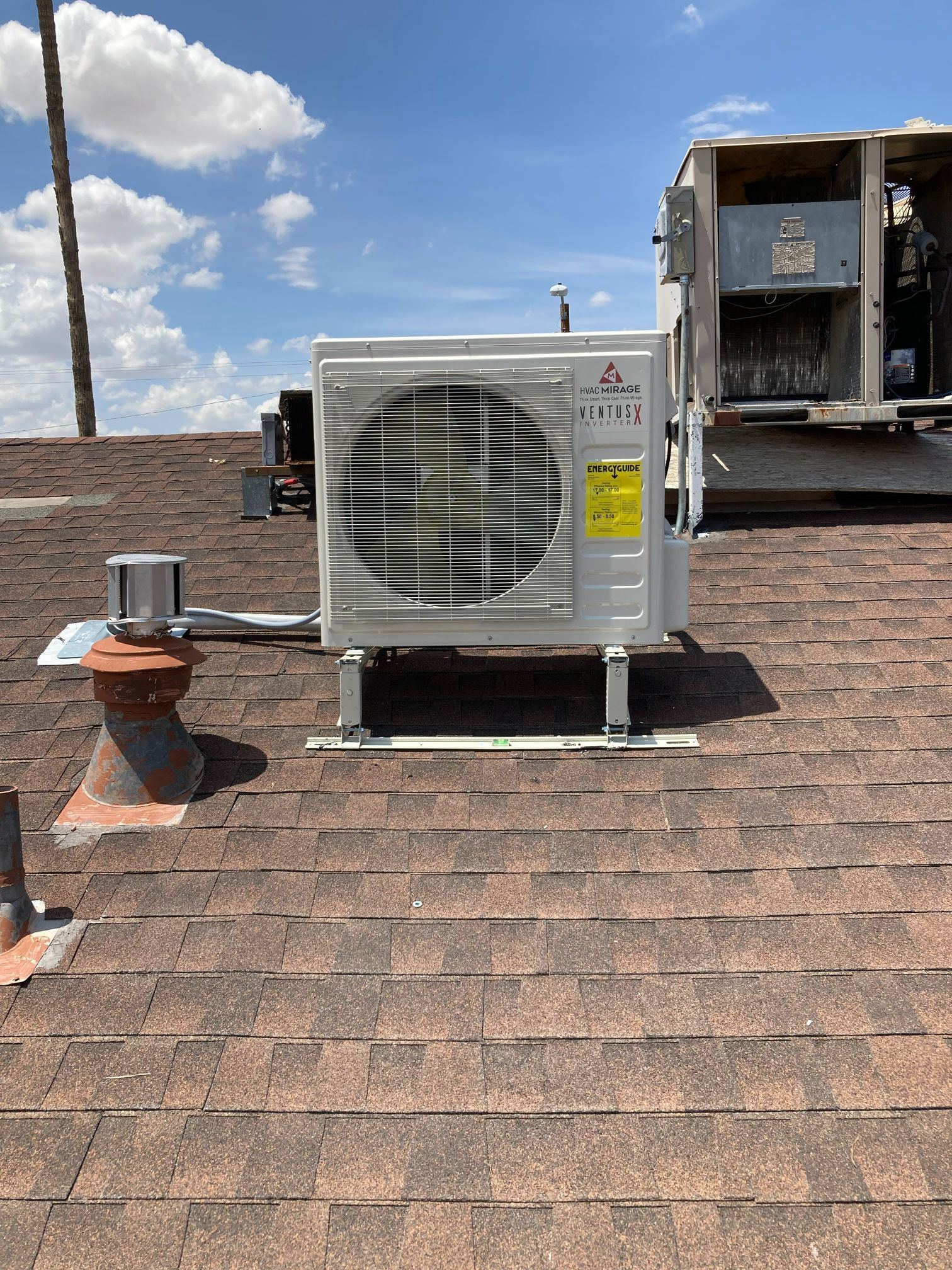 A white Mitsubishi air conditioning unit sits on a brown rooftop under a blue sky.