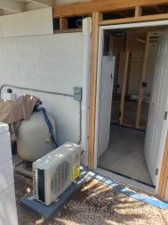 Exterior with a white wall, pool equipment, and an open doorway to a room under construction.
