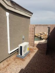 An air conditioning unit on a gravel patio beside a building with a pool visible in the background.