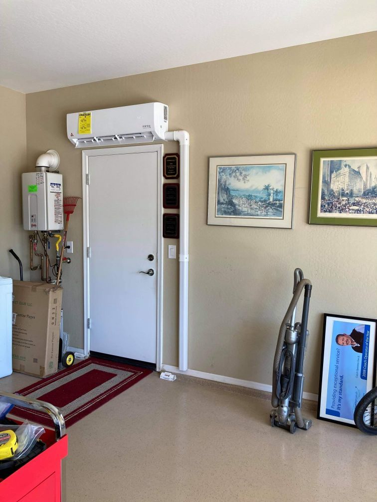 Garage interior with door, AC unit, water heater, art, vacuum, and red rug. Beige walls and floor.