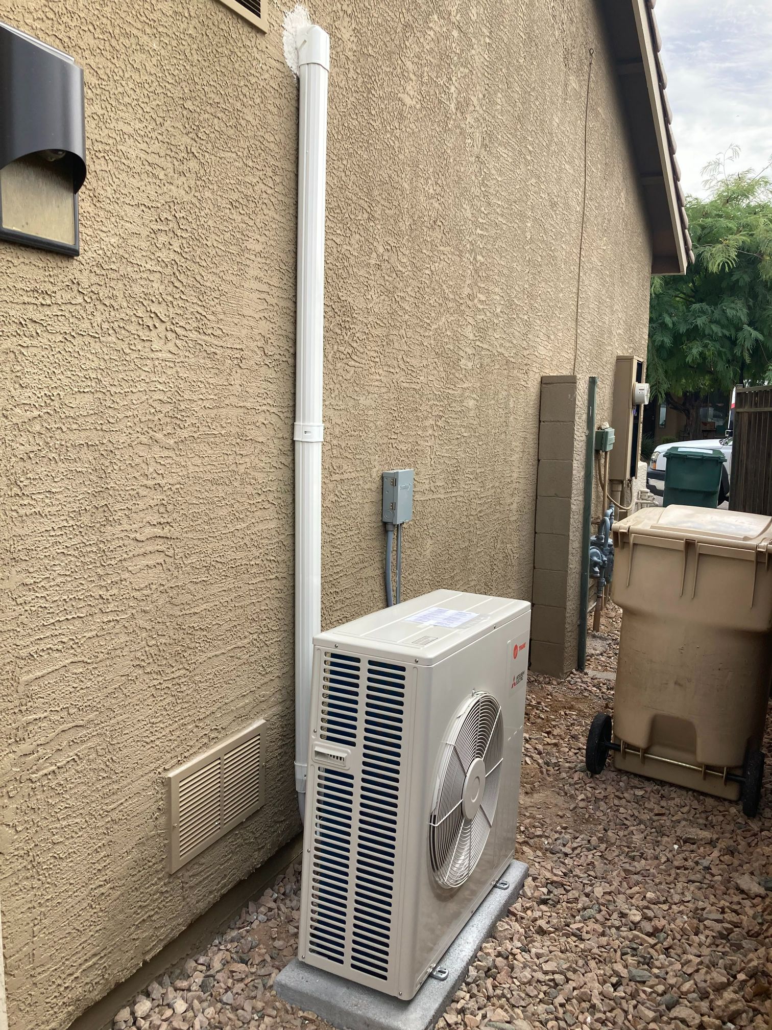Air conditioning unit outside a stucco building with a vent pipe.