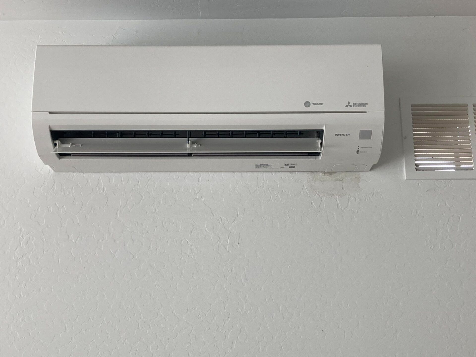White Mitsubishi ductless air conditioner mounted on white wall.