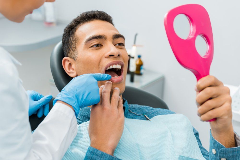 A Man is Sitting in a Dental Chair Looking at His Teeth — Ballina Denture Clinic Michael J Parker in Lennox Head, NSW