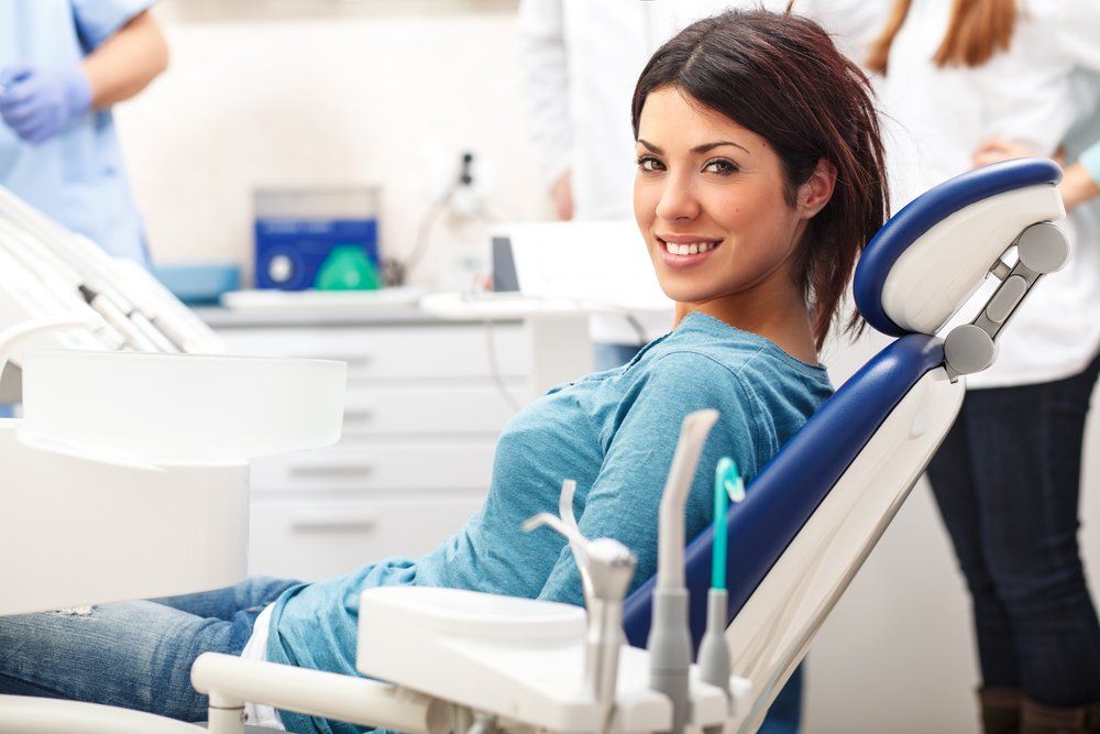 A Woman is Sitting in a Dental Chair and Smiling — Ballina Denture Clinic Michael J Parker in Alstonville, NSW