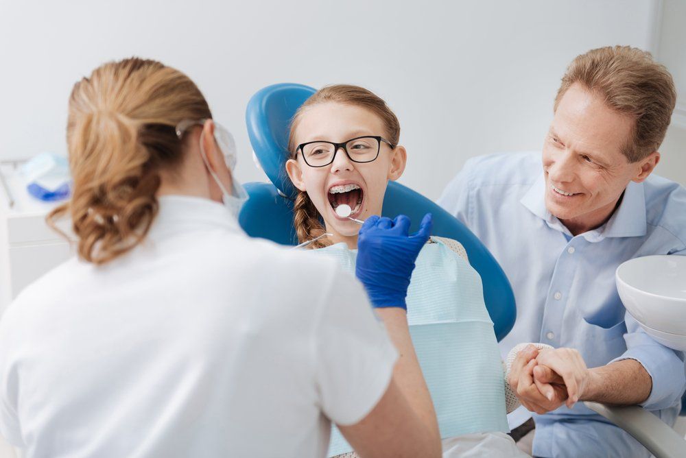A Little Girl is Sitting in a Dental Chair With Her Mouth Open — Ballina Denture Clinic Michael J Parker in Byron Bay, NSW