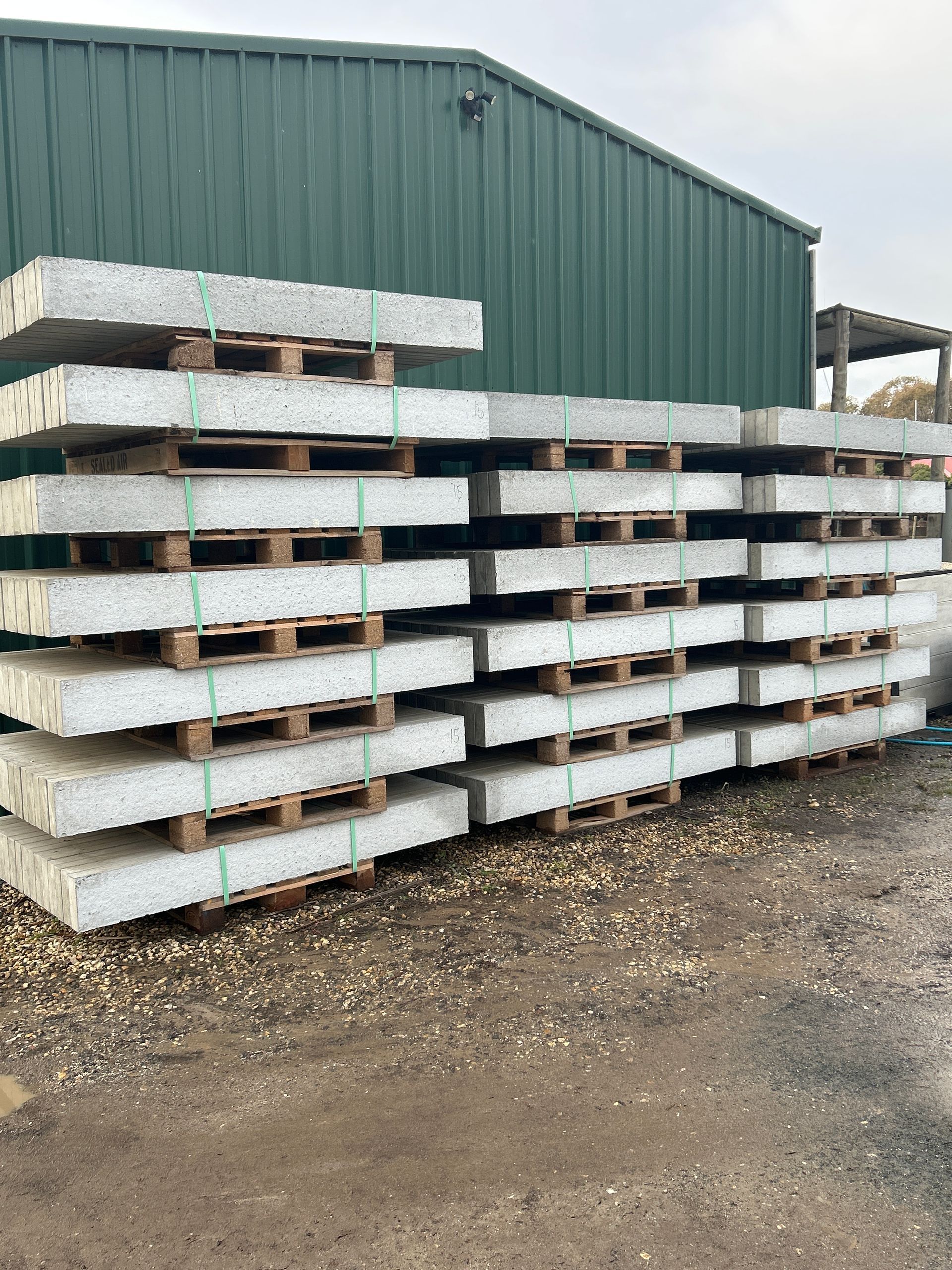 A stack of concrete slabs on wooden pallets in front of a green building. — Wodonga Sand & Soil in Wodonga, VIC