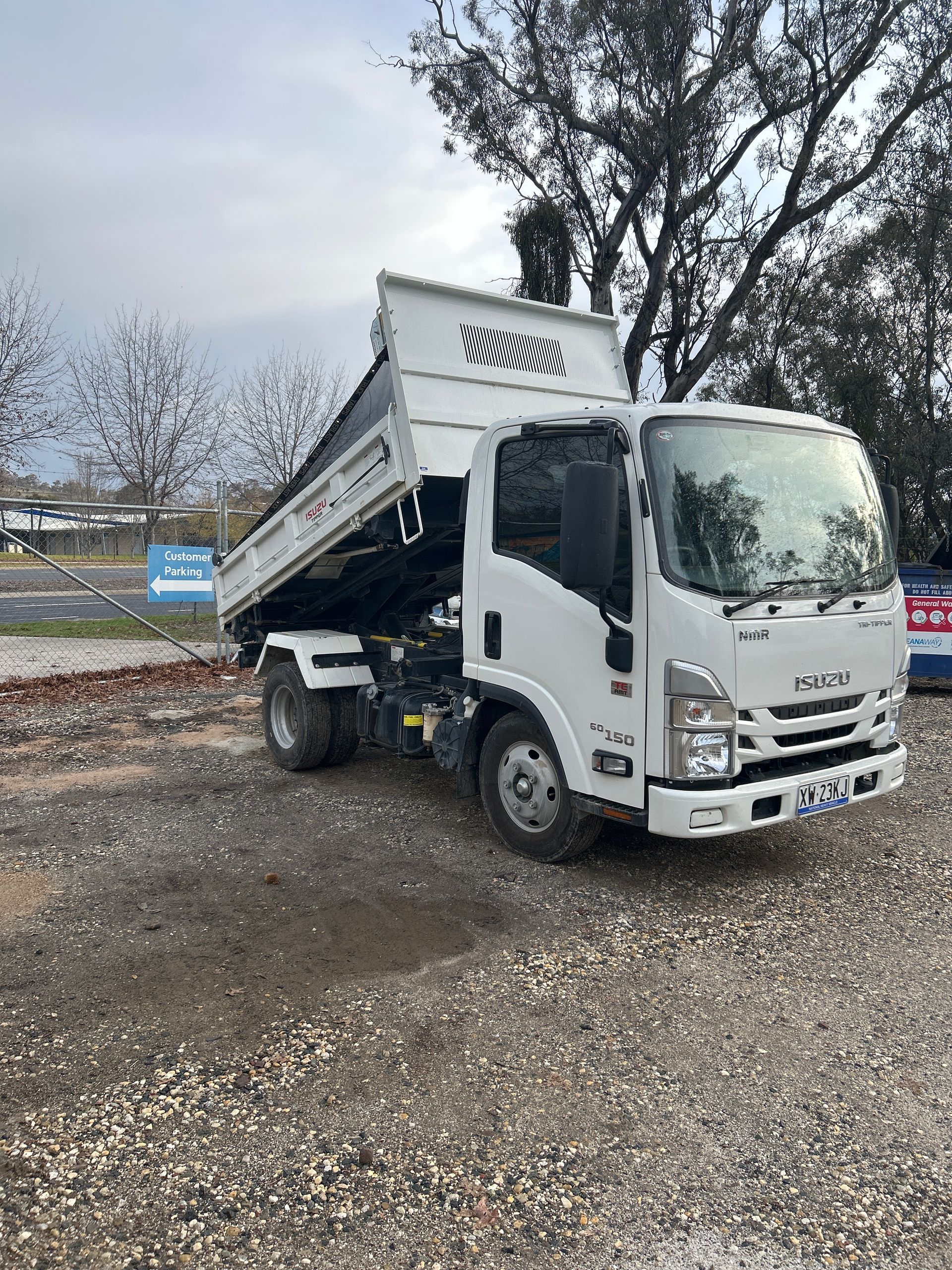White Isuzu dump truck, bed raised, parked on gravel. Cloudy sky, bare trees in the background. — Wodonga Sand & Soil in Wodonga, VIC