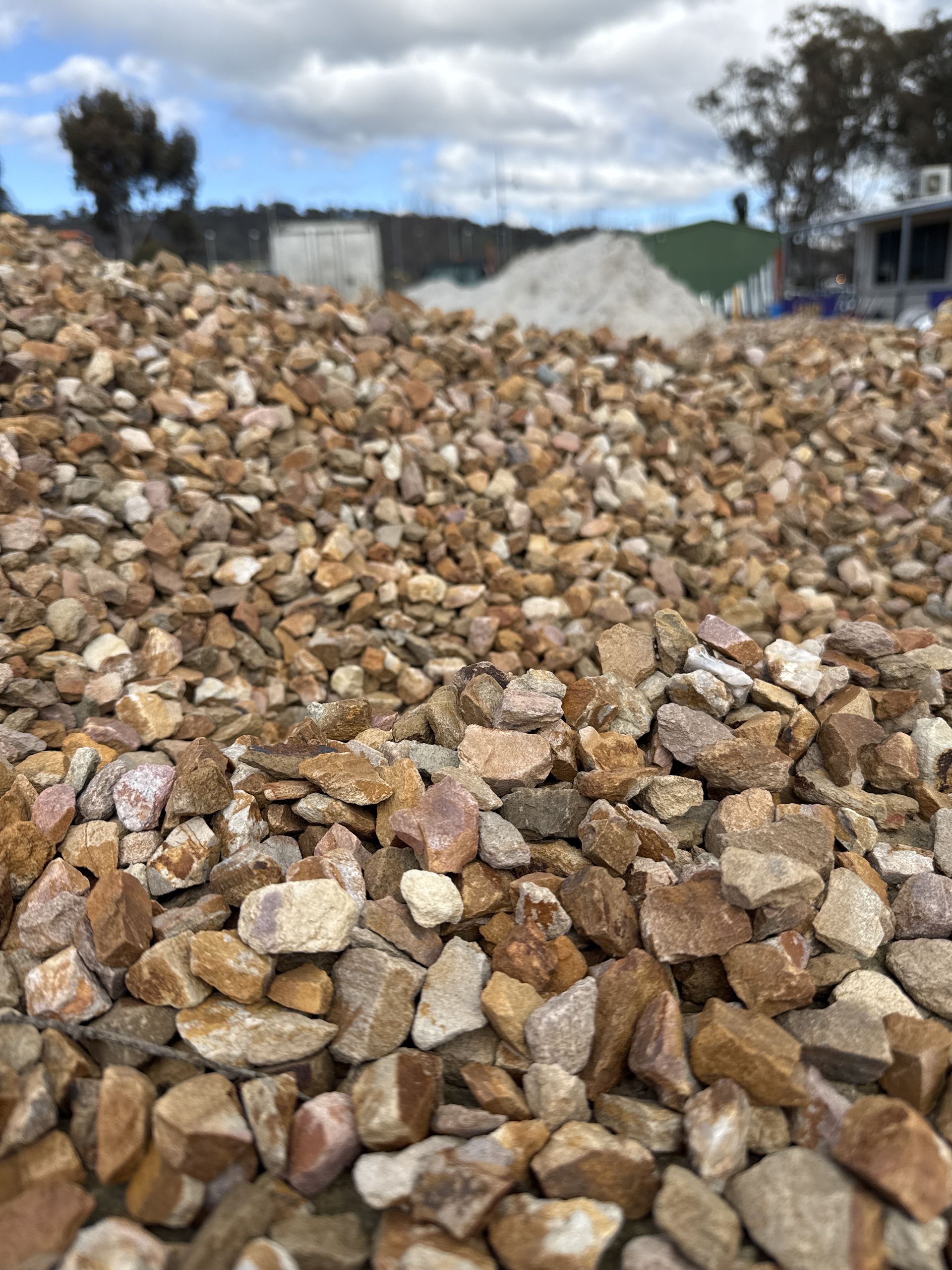 Close-up Of A Pile Of Tan And Brown Gravel Against A Blurred Background Of A Cloudy Sky And Buildings — Wodonga Sand & Soil in Wodonga, VIC