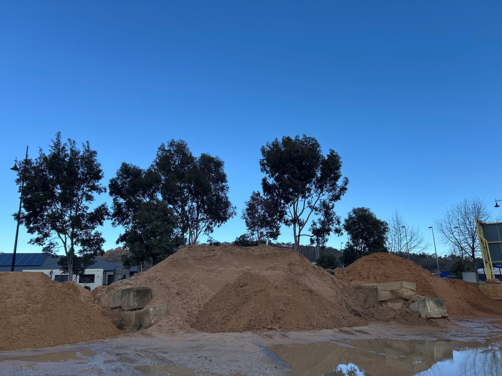 Piles of tan dirt and gravel in front of a row of trees against a clear blue sky. — Wodonga Sand & Soil in Wodonga, VIC