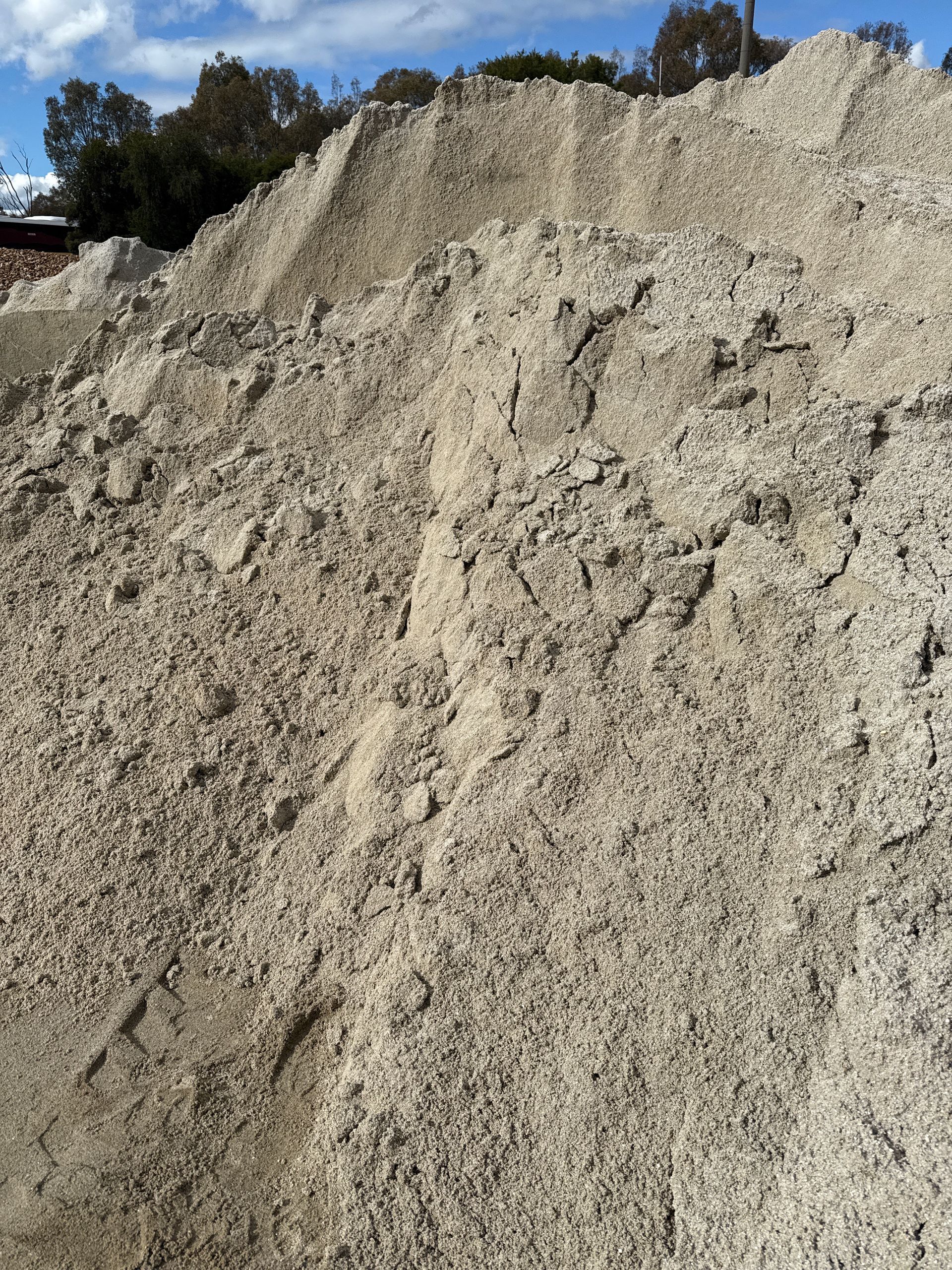 Large pile of light-colored sand or gravel against a background of trees and blue sky. — Wodonga Sand & Soil in Wodonga, VIC