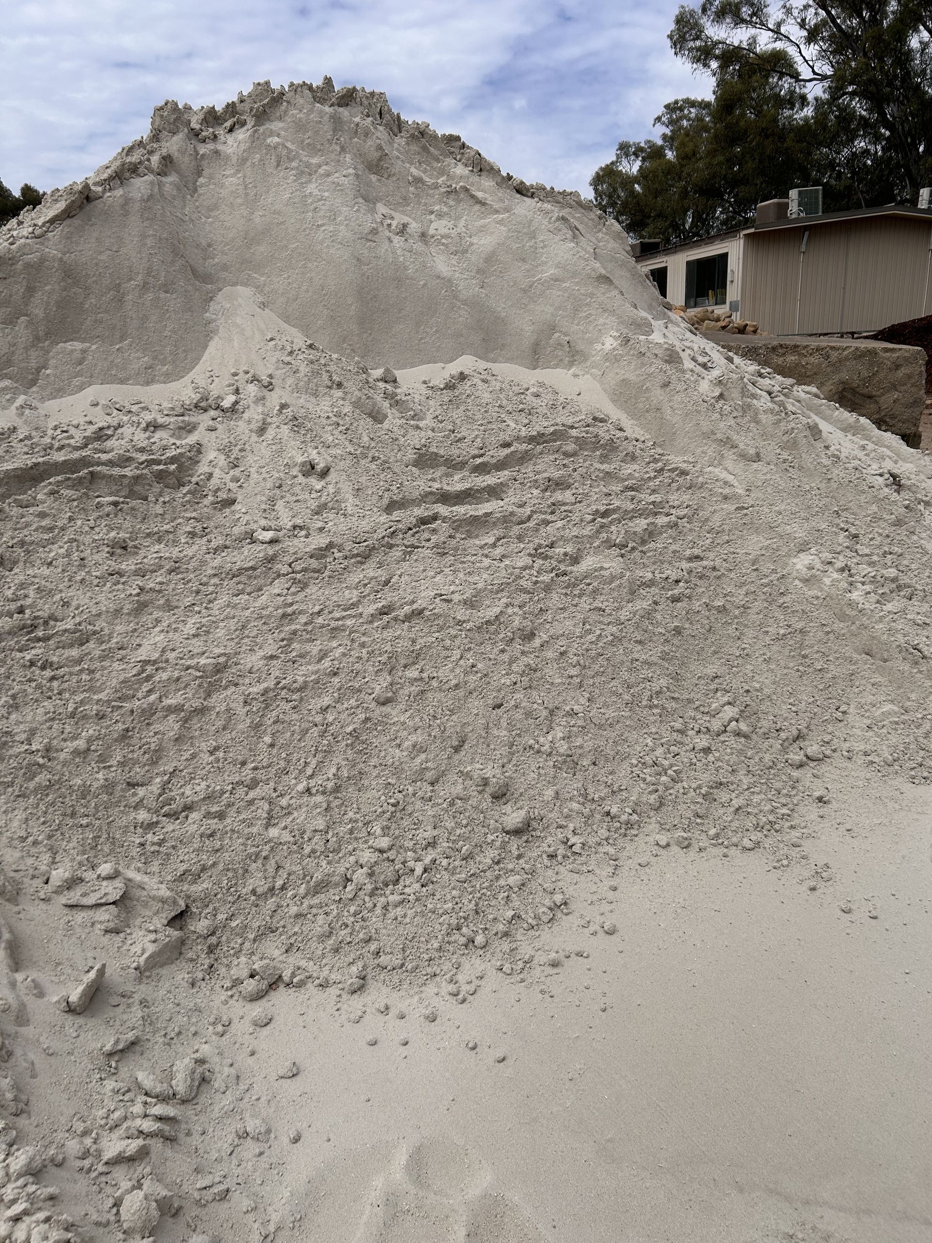 Pile of light-colored sand. A house is visible in the background — Wodonga Sand & Soil in Wodonga, VIC